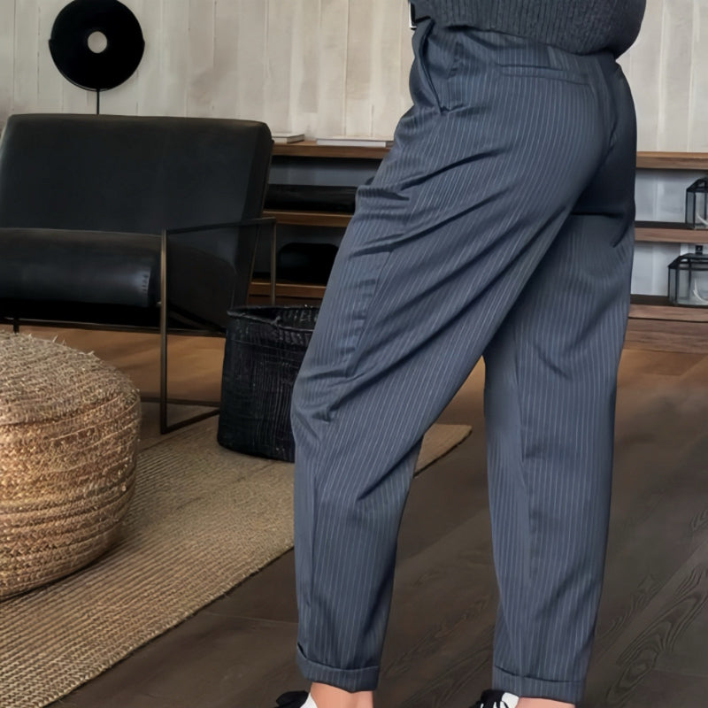 Pantaloni a righe grigie eleganti in un salotto moderno con mobili scuri e tappeto intrecciato. Stile formale, moda uomo, design contemporaneo.
