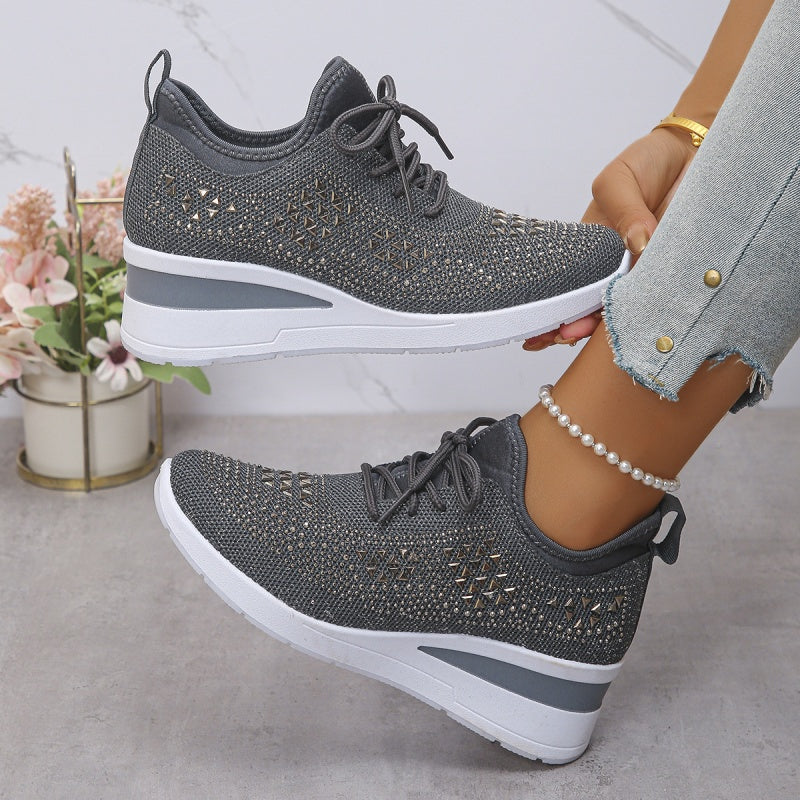 Scarpe da ginnastica grigie da donna con suola bianca, dettagli traforati, indossate con jeans chiari. Sfondo con fiori decorativi.