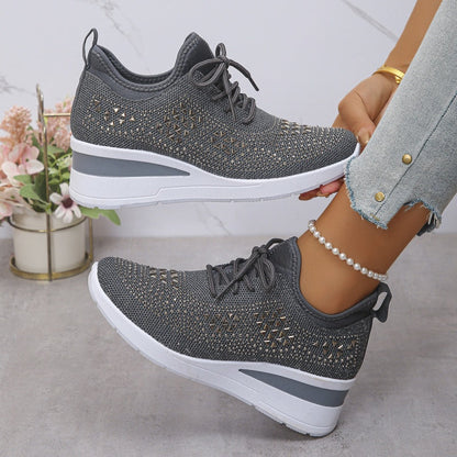 Scarpe da ginnastica grigie da donna con suola bianca, dettagli traforati, indossate con jeans chiari. Sfondo con fiori decorativi.