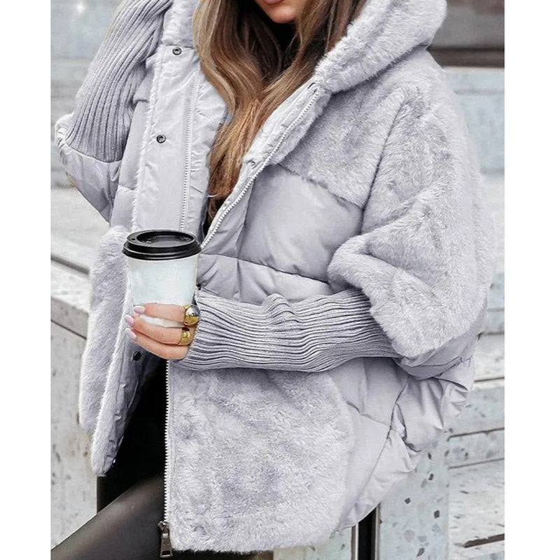 Giacca invernale donna in pelliccia sintetica grigia con cappuccio, abbinata a maglione a coste, mentre tiene una tazza di caffè. Moda autunno inverno.