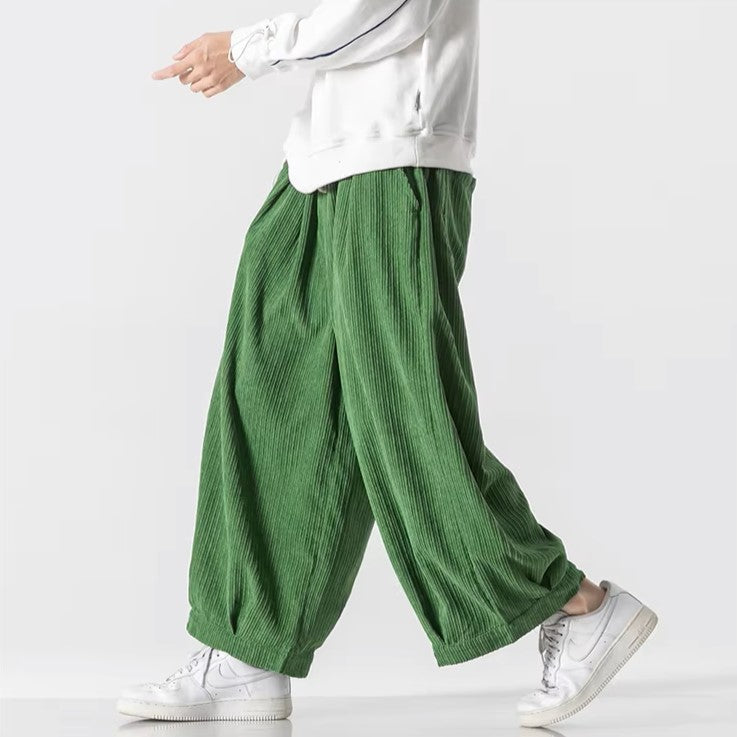 Pantaloni larghi verdi in tessuto plissettato, indossati con felpa bianca e sneakers bianche. Moda casual uomo, stile confortevole e moderno.
