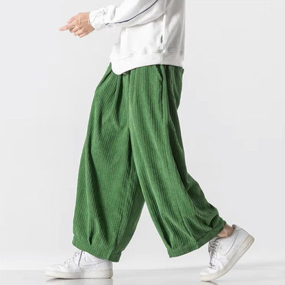 Pantaloni larghi verdi in tessuto plissettato, indossati con felpa bianca e sneakers bianche. Moda casual uomo, stile confortevole e moderno.