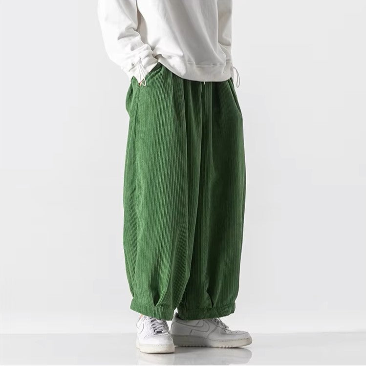 Pantaloni larghi verdi in velluto a coste, indossati con felpa bianca e sneakers bianche. Moda casual uomo, stile streetwear moderno.