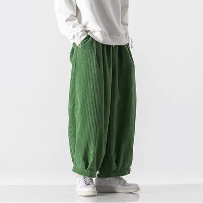 Pantaloni larghi verdi in velluto a coste, indossati con felpa bianca e sneakers bianche. Moda casual uomo, stile streetwear moderno.