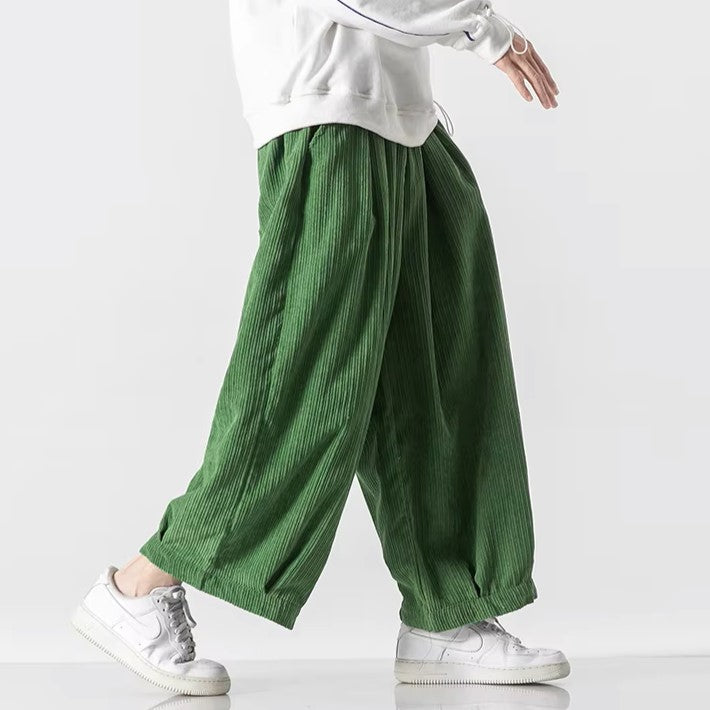 Pantaloni verdi a coste larghe, indossati con felpa bianca e sneakers bianche. Moda casual, stile urbano, abbigliamento comodo.