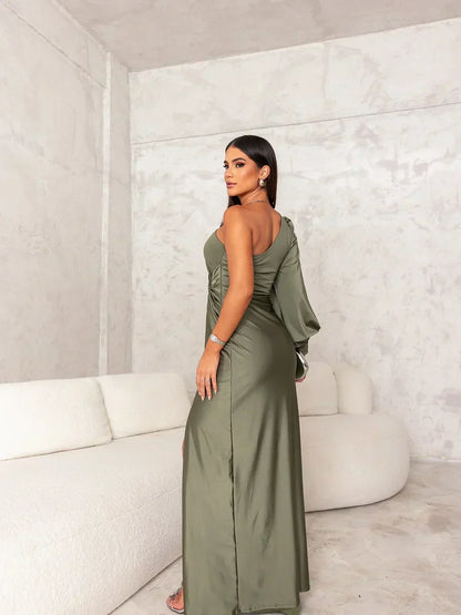 Donna in abito lungo verde oliva elegante, posa in un salotto moderno con divano bianco. Moda femminile, abbigliamento da sera, stile sofisticato.
