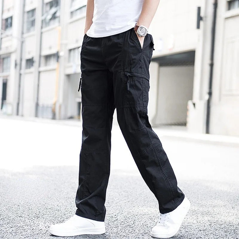 Pantaloni cargo neri da uomo, stile casual, con tasche laterali, indossati con scarpe bianche su sfondo urbano. Moda maschile contemporanea.