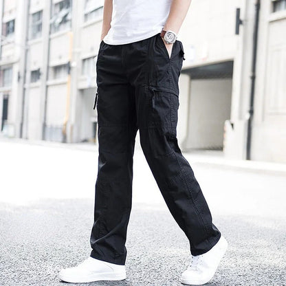 Pantaloni cargo neri da uomo, stile casual, con tasche laterali, indossati con scarpe bianche su sfondo urbano. Moda maschile contemporanea.
