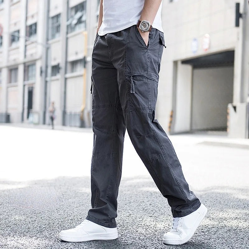 Pantaloni cargo grigi da uomo, stile casual, con tasche multiple, indossati con scarpe bianche su strada urbana. Moda maschile contemporanea.