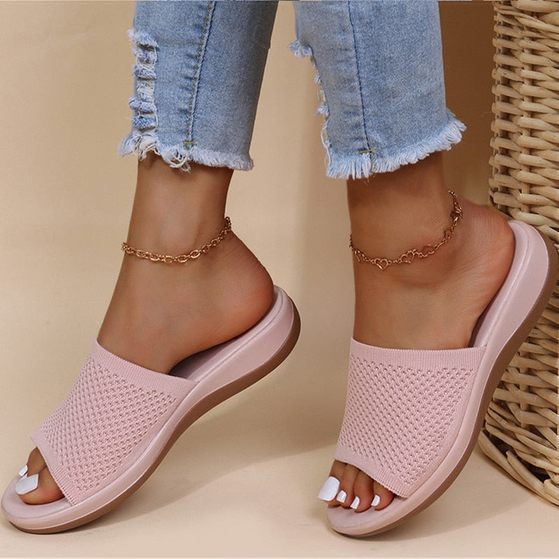 Sandali rosa intrecciati su piedi femminili con jeans strappati e cavigliere dorate, moda estiva casual, calzature comode eleganti.