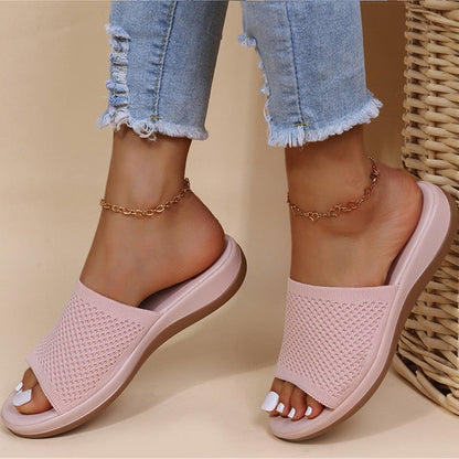 Sandali rosa intrecciati su piedi femminili con jeans strappati e cavigliere dorate, moda estiva casual, calzature comode eleganti.