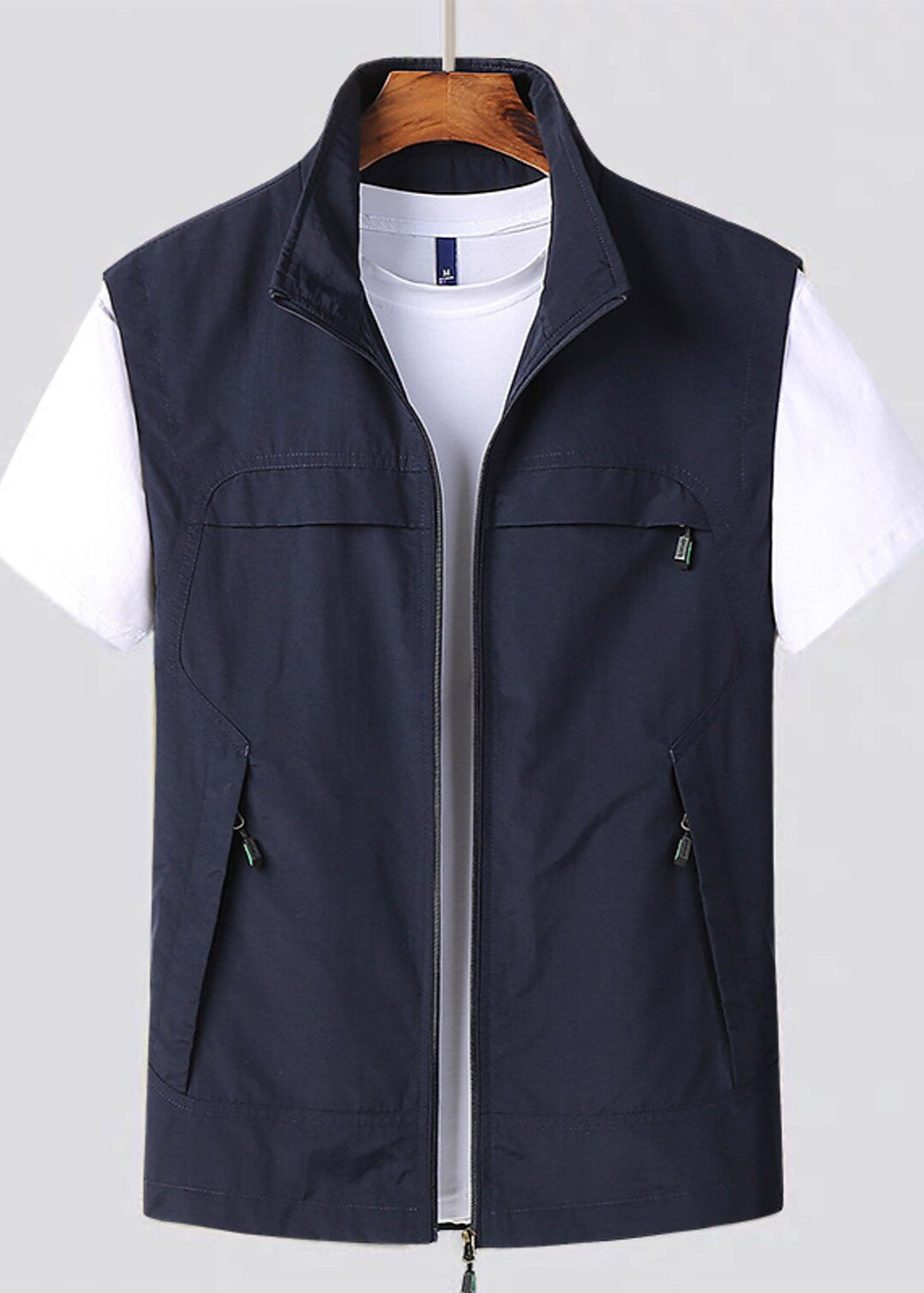 Gilet blu scuro da uomo su gruccia, con zip e tasche, sopra una maglietta bianca. Abbigliamento casual, moda maschile, stile versatile.