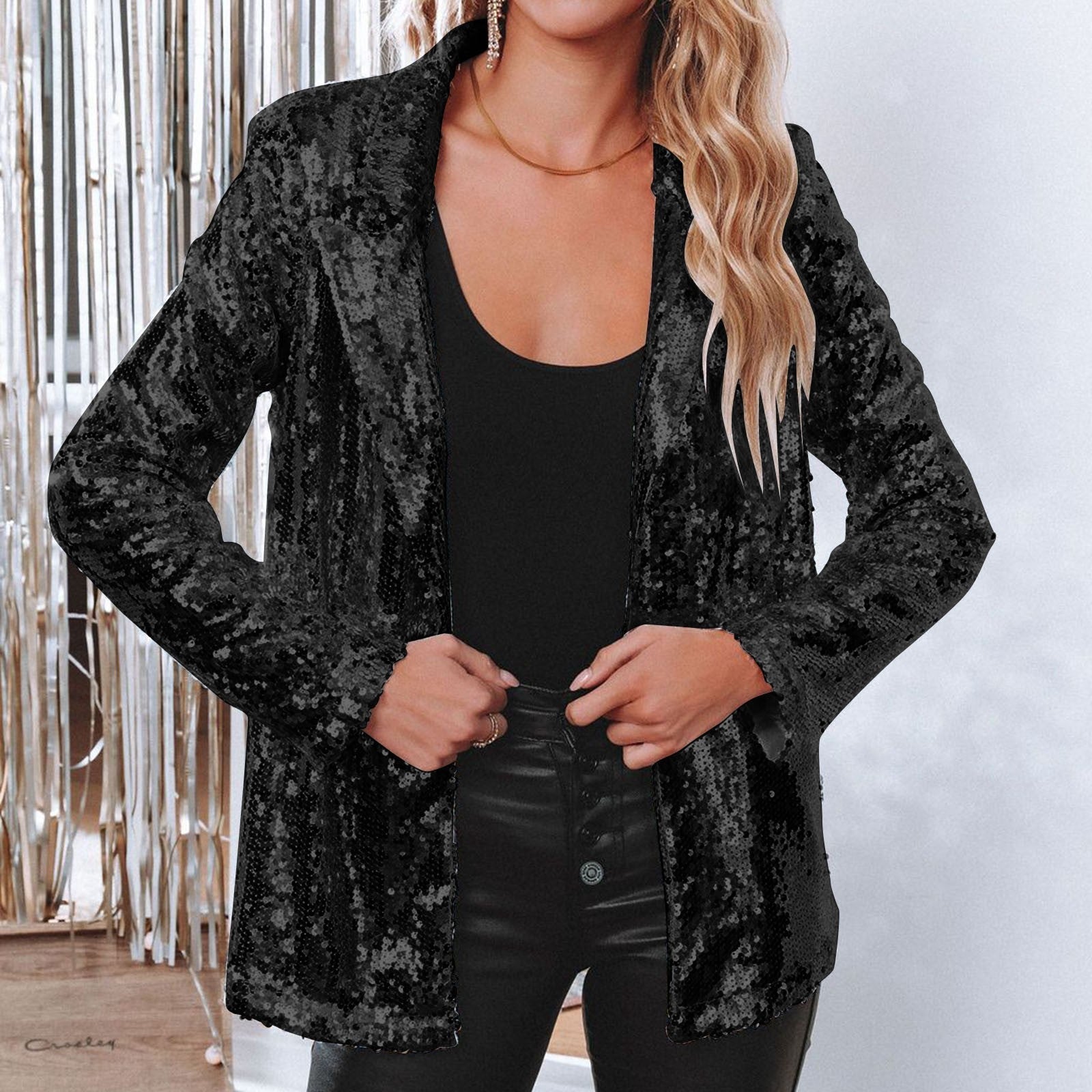 Donna con giacca di paillettes nere, top nero e pantaloni in pelle, sfondo con decorazioni argentate. Moda elegante, abbigliamento da festa.