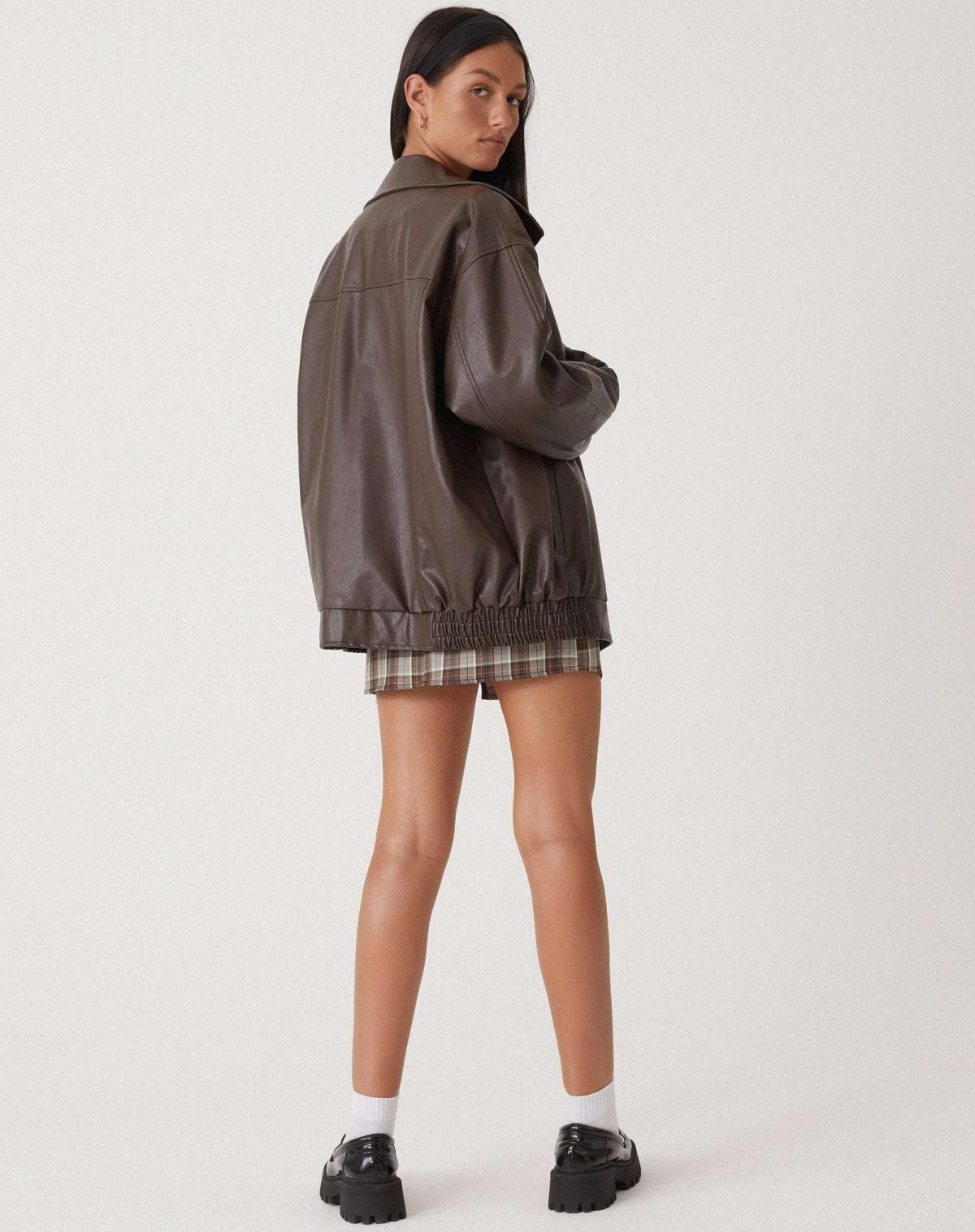 Donna con giacca di pelle marrone oversize, gonna a quadri, calze bianche e scarpe nere. Moda autunnale, stile casual chic.